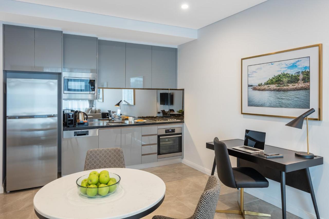 Meriton Suites Sussex Street, Sydney Ngoại thất bức ảnh The photo shows a modern kitchen and dining area in an apartment. The kitchen features sleek gray cabinetry, a stainless steel fridge, and a microwave. There is a countertop with cooking appliances, including an oven and stovetop. A small round dinin