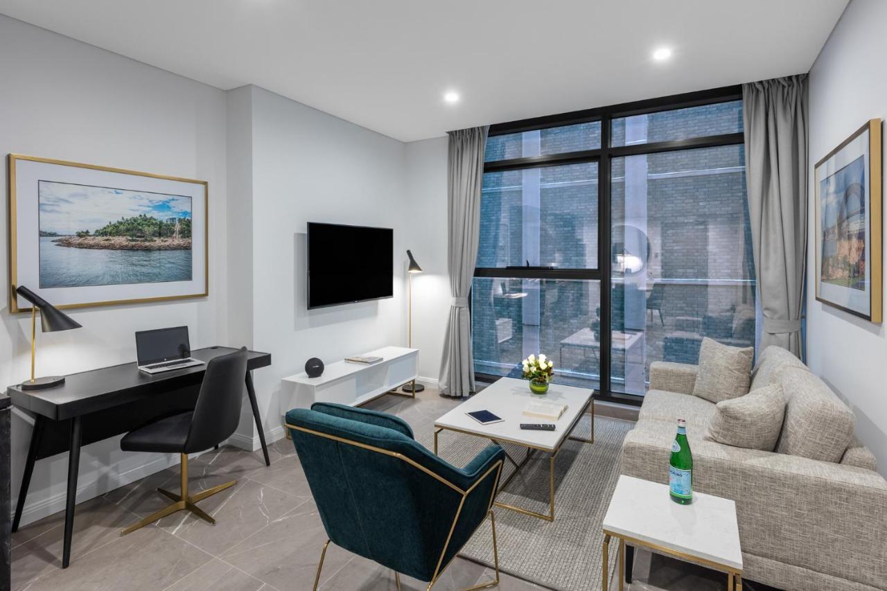 Meriton Suites Sussex Street, Sydney Ngoại thất bức ảnh The photo shows a modern living area with a light color scheme. There is a comfortable seating arrangement that includes a beige sofa and an accent chair in teal. A coffee table is positioned in front of the sofa, with a small vase of flowers on it. 