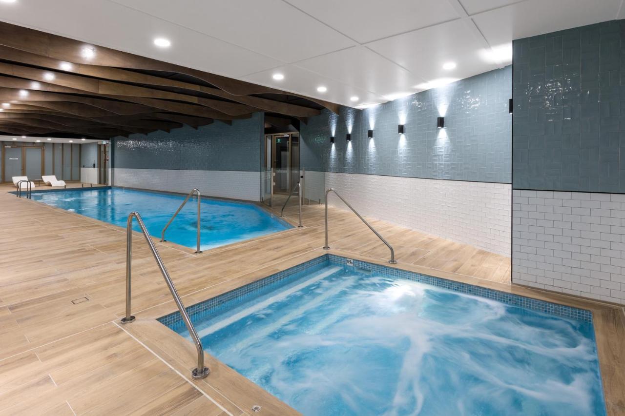 Meriton Suites Sussex Street, Sydney Ngoại thất bức ảnh The photo shows a modern indoor spa area. There are two pools: one is larger and has a clear blue water, while the other is smaller, possibly a hot tub, with jets creating bubbles. The walls are a mix of blue tiles and white tiles, and the floor is m