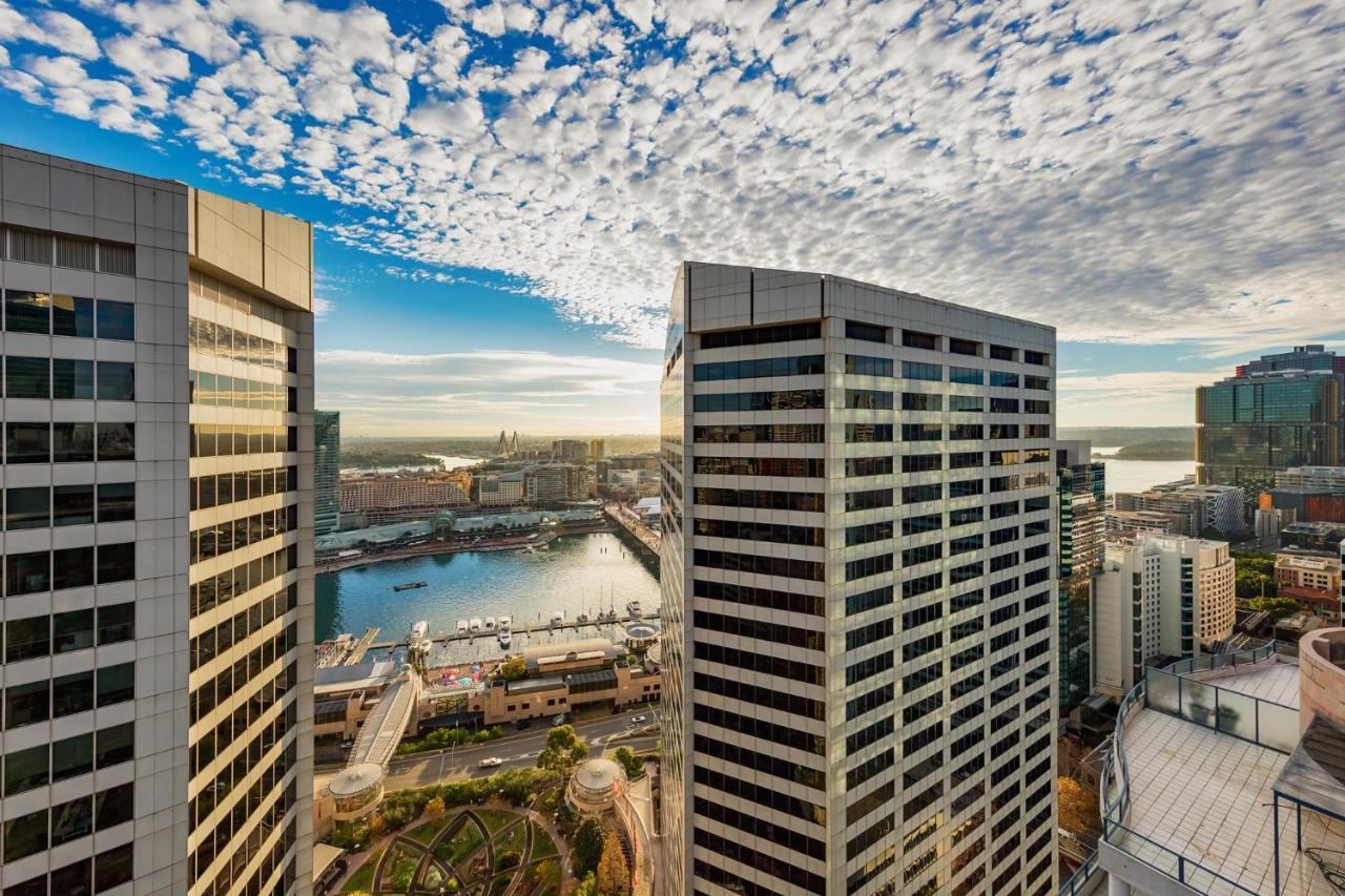 Meriton Suites Sussex Street, Sydney Ngoại thất bức ảnh The photo depicts a panoramic view of a modern cityscape featuring tall commercial buildings with glass facades. The shot is taken from a height, showing the intricate architecture of the nearby structures. Below, there is a body of water, which appe