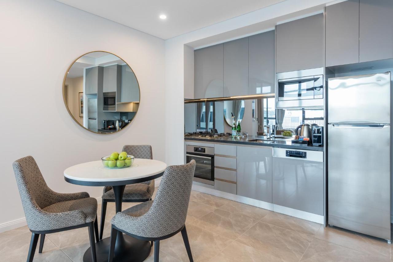 Meriton Suites Sussex Street, Sydney Ngoại thất bức ảnh The photo features a modern kitchen and dining area. The kitchen has sleek grey cabinets and countertops, with built-in appliances including an oven and possibly a cooktop. There's a large stainless steel refrigerator on the right. A round dining tab