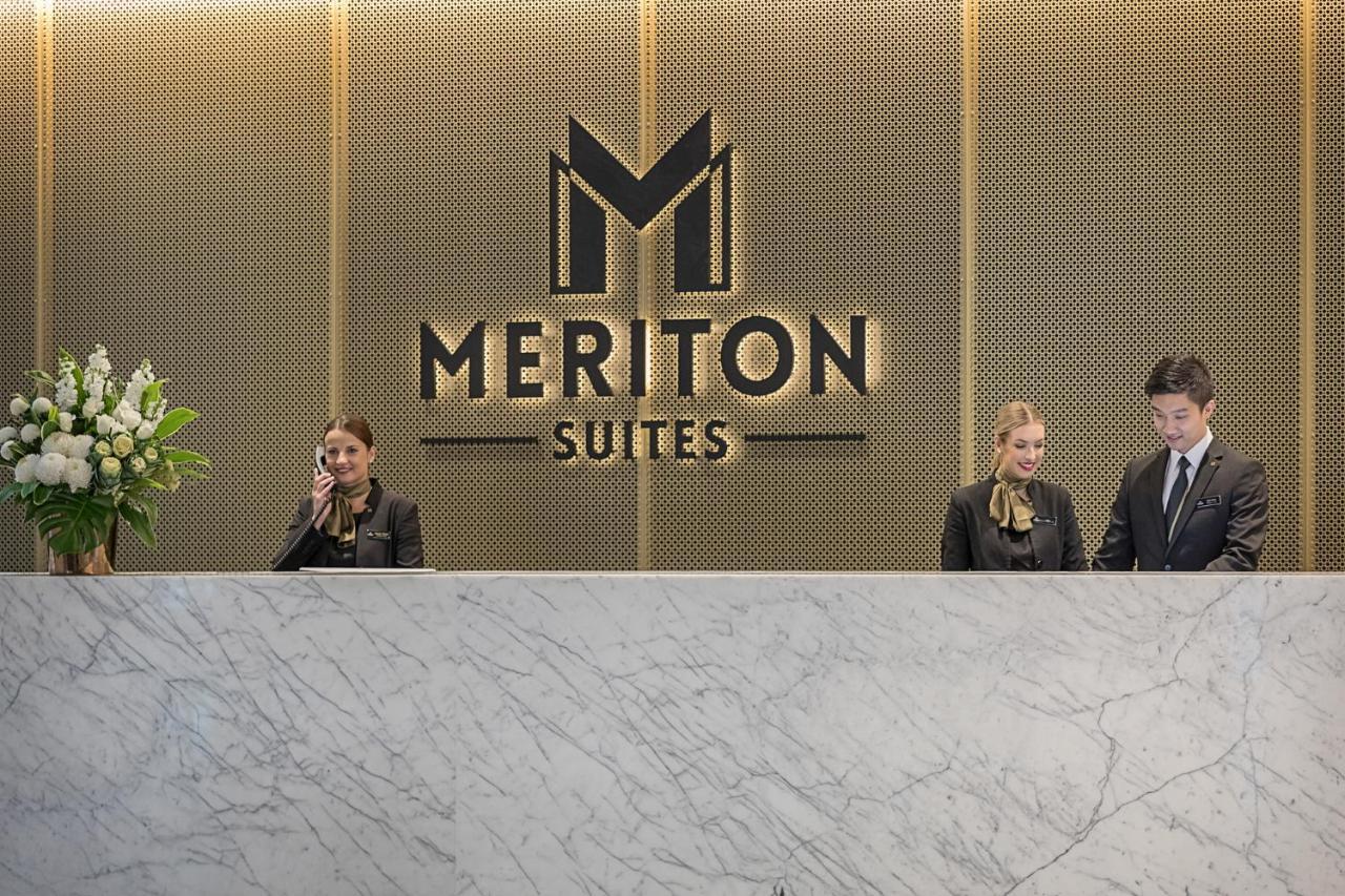Meriton Suites Sussex Street, Sydney Ngoại thất bức ảnh The photo depicts the reception area of a hotel called "Meriton Suites." In the background, there is a large, illuminated sign featuring the hotel’s logo. The reception desk is made of marble and is staffed by two individuals dressed in professional 