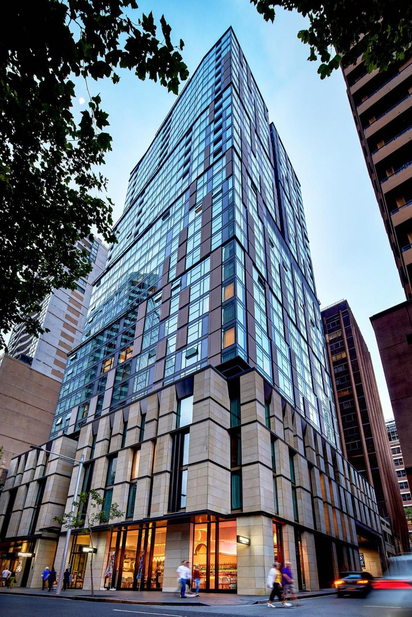 Meriton Suites Sussex Street, Sydney Ngoại thất bức ảnh The photo shows a modern high-rise building with a sleek, glass facade reflecting its surroundings. The structure features a combination of glass and concrete materials, with multiple stories visible. The lower part of the building has a sturdy, text