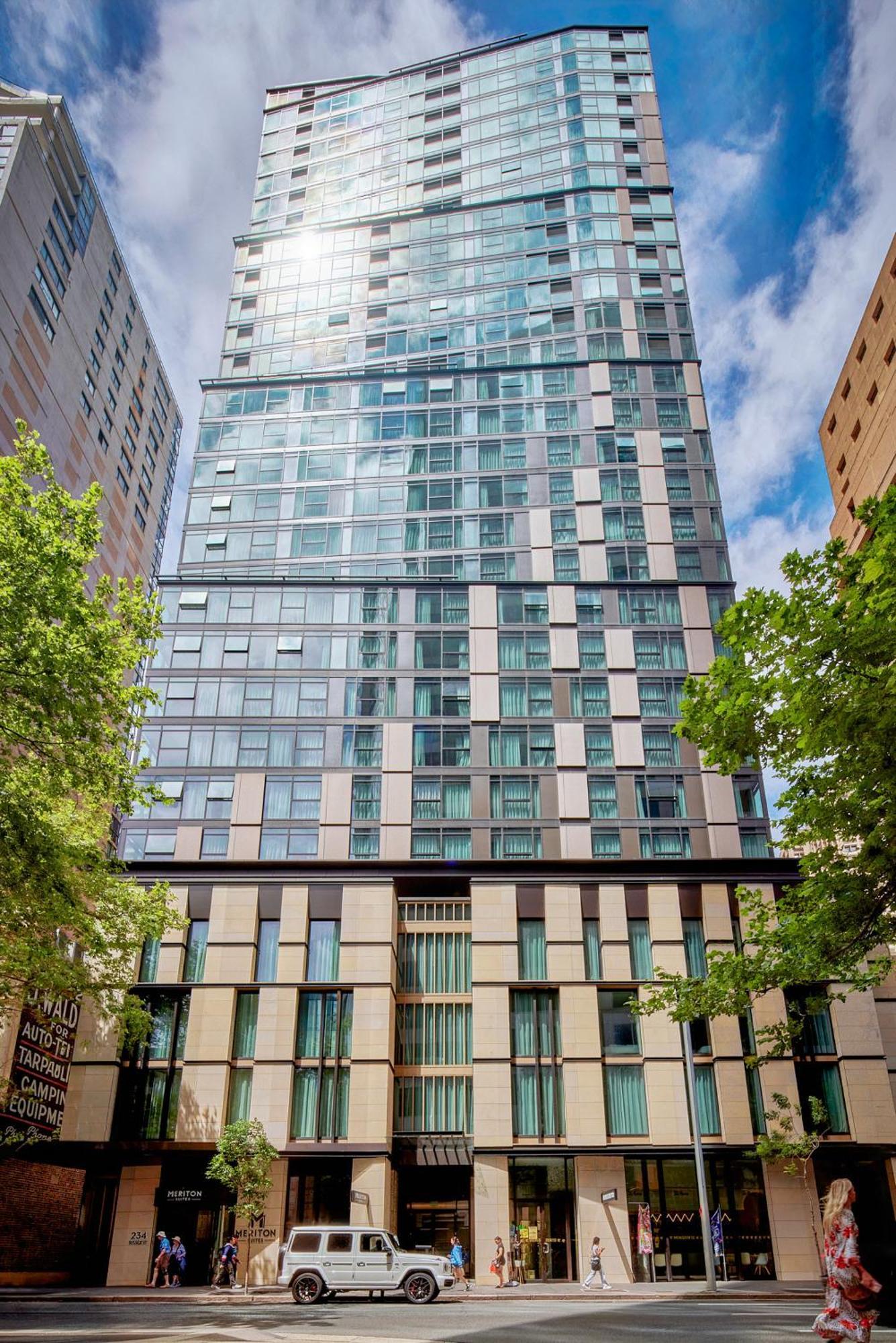 Meriton Suites Sussex Street, Sydney Ngoại thất bức ảnh The photo shows a tall modern building with a glass facade and various architectural design elements. The structure has multiple stories, with large windows that reflect the surrounding environment. At the base, there are sections that appear to have